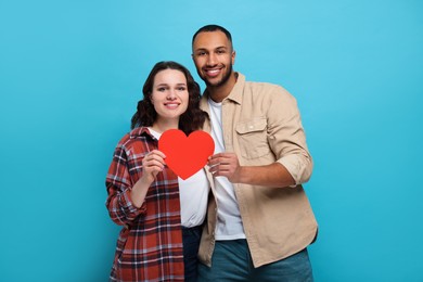 Photo of Lovely couple with red paper heart on light blue background. Valentine's day celebration