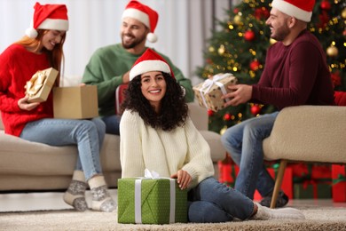 Photo of Christmas celebration in circle of friends. Happy young woman with gift box at home, selective focus