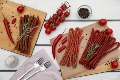 Photo of Delicious kabanosy with rosemary, peppercorn, chilli and tomatoes on white wooden table, flat lay