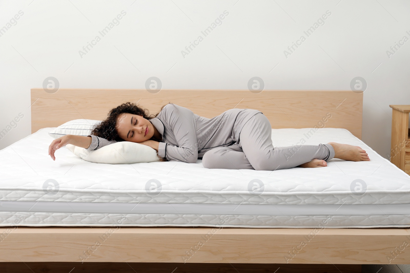 Photo of Young African American woman sleeping on bed with comfortable mattress and pillow at home