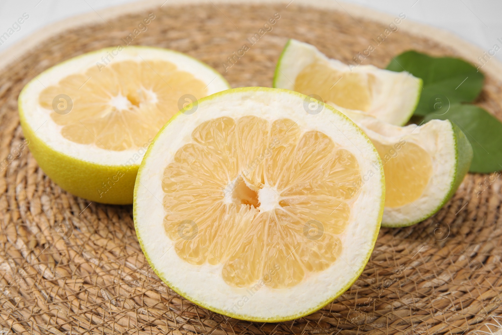 Photo of Cut sweetie fruits with green leaves on wicker mat, closeup