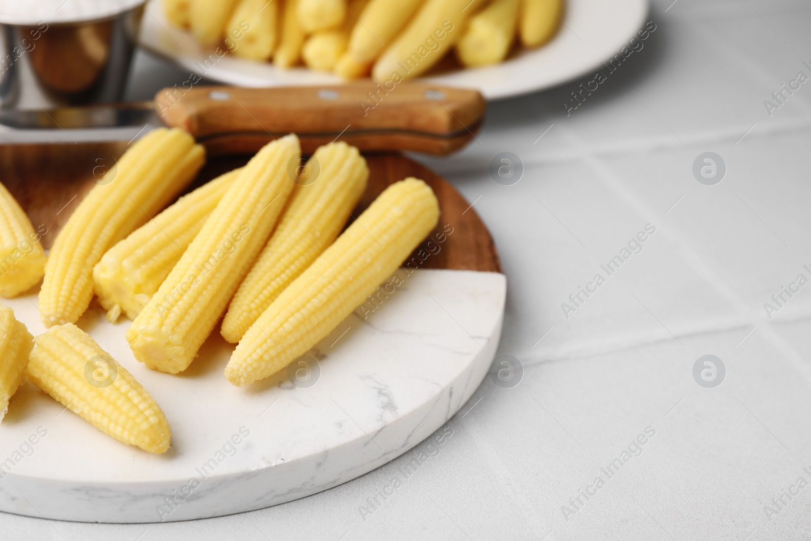 Photo of Tasty fresh yellow baby corns and knife on white tiled table, closeup. Space for text