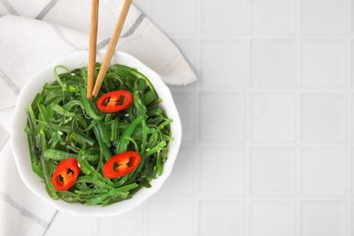 Tasty seaweed salad served in bowl on white tiled table, top view. Space for text