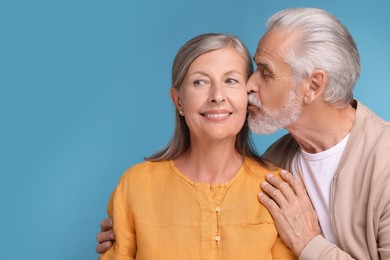 Photo of Senior man kissing his beloved woman on light blue background, space for text