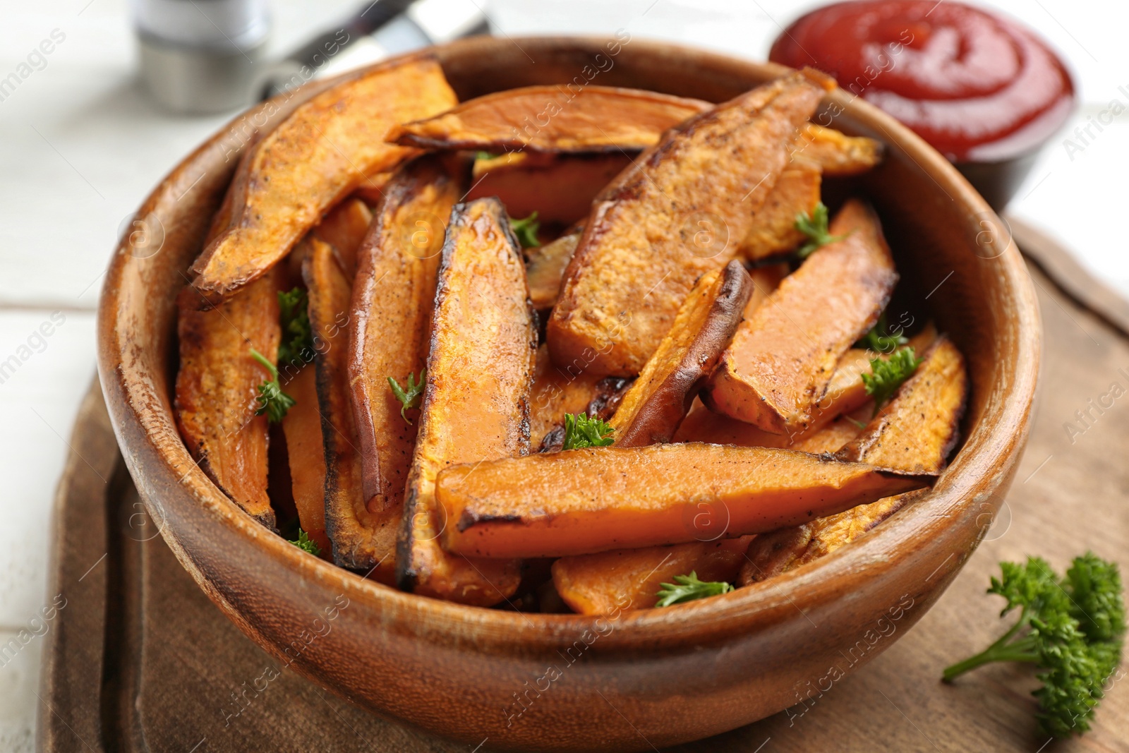 Photo of Bowl with tasty sweet potato fries on wooden board, closeup