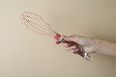 Woman holding whisk on beige background, closeup