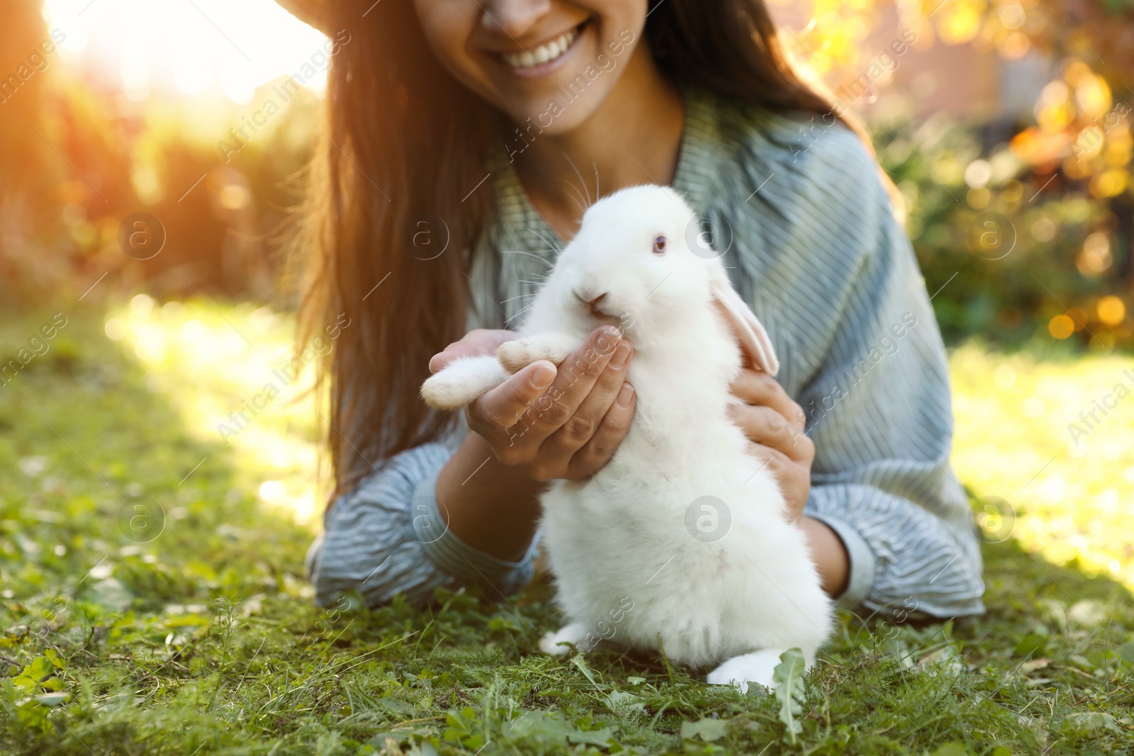 Photo of Happy woman with cute rabbit on green grass outdoors, closeup