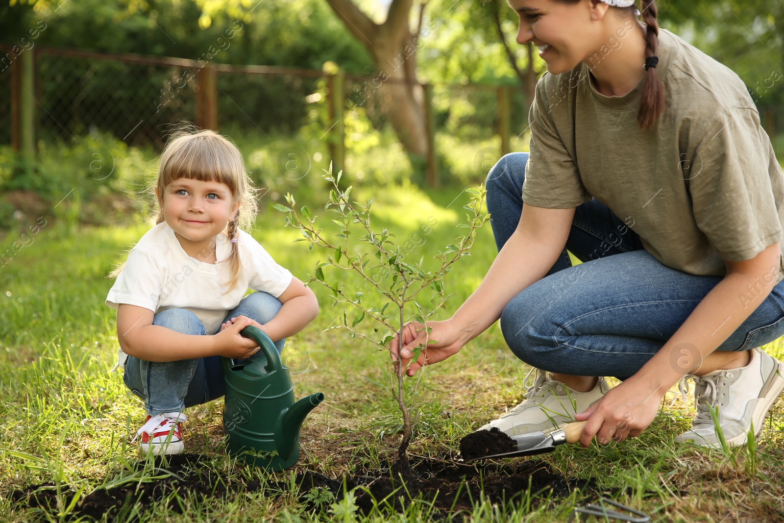 Photo of Mother and her daughter planting tree together in garden