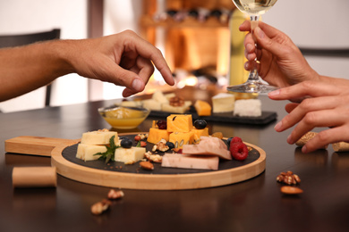 Couple with different types of delicious cheeses at table indoors, closeup