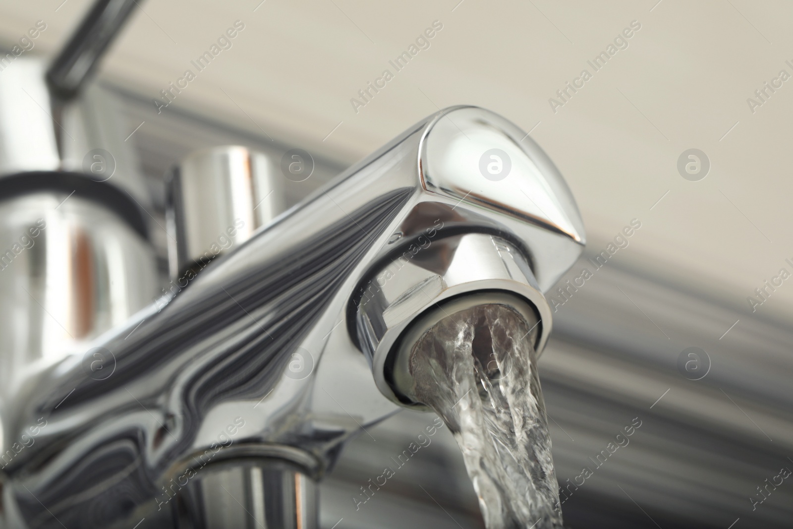 Photo of Water flowing from bath tap on blurred background, closeup