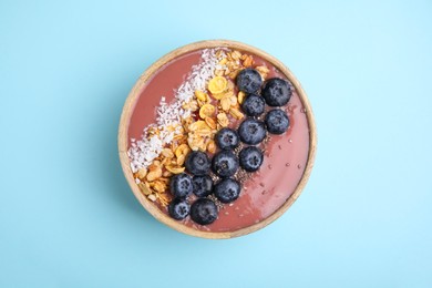 Photo of Bowl of delicious fruit smoothie with fresh blueberries, granola and coconut flakes on light blue background, top view