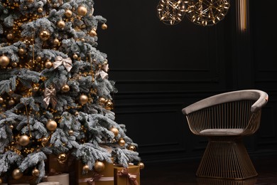 Photo of Beautiful decorated Christmas tree, chair and festive decor in dark room. Interior design