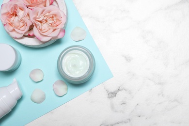 Photo of Flat lay composition with different skin care products and flowers on white marble background, space for text