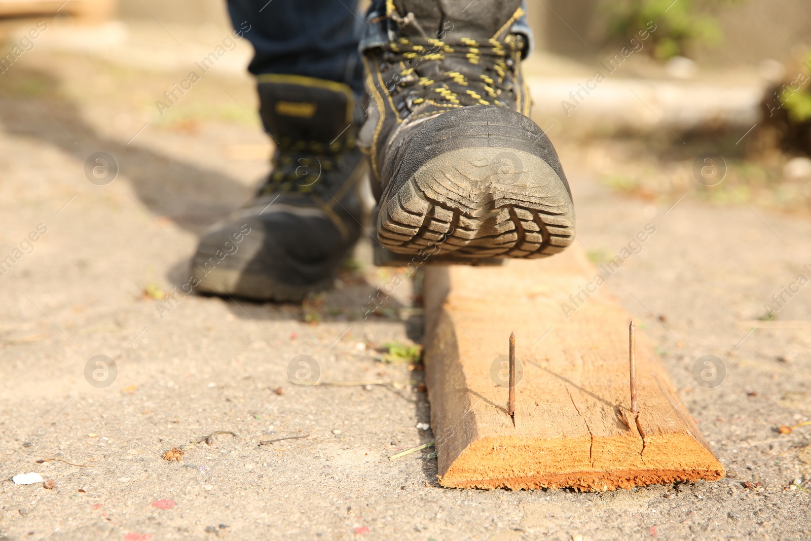 Photo of Careless worker stepping on nail in wooden plank outdoors, closeup