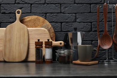 Photo of Wooden cutting boards, utensils, moka pot and cup on gray table near dark brick wall