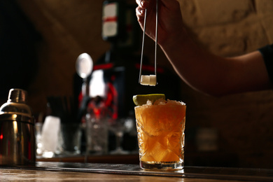 Photo of Bartender decorating glass of fresh alcoholic cocktail at bar counter, closeup. Space for text