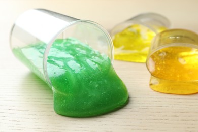 Overturned plastic containers with bright slimes on wooden background, closeup