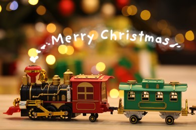 Image of Greeting card with phrase Merry Christmas. Toy locomotive with rising steam in form of phrase Merry Christmas on wooden table against blurred lights