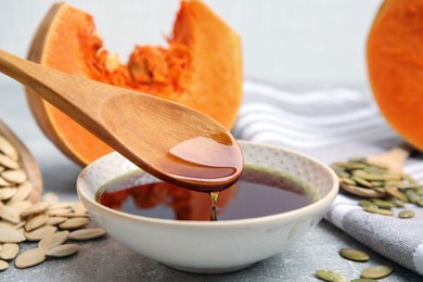 Photo of Wooden spoon with pumpkin oil over bowl and seeds on table, closeup