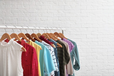 Wardrobe rack with stylish clothes near brick wall indoors. Space for text