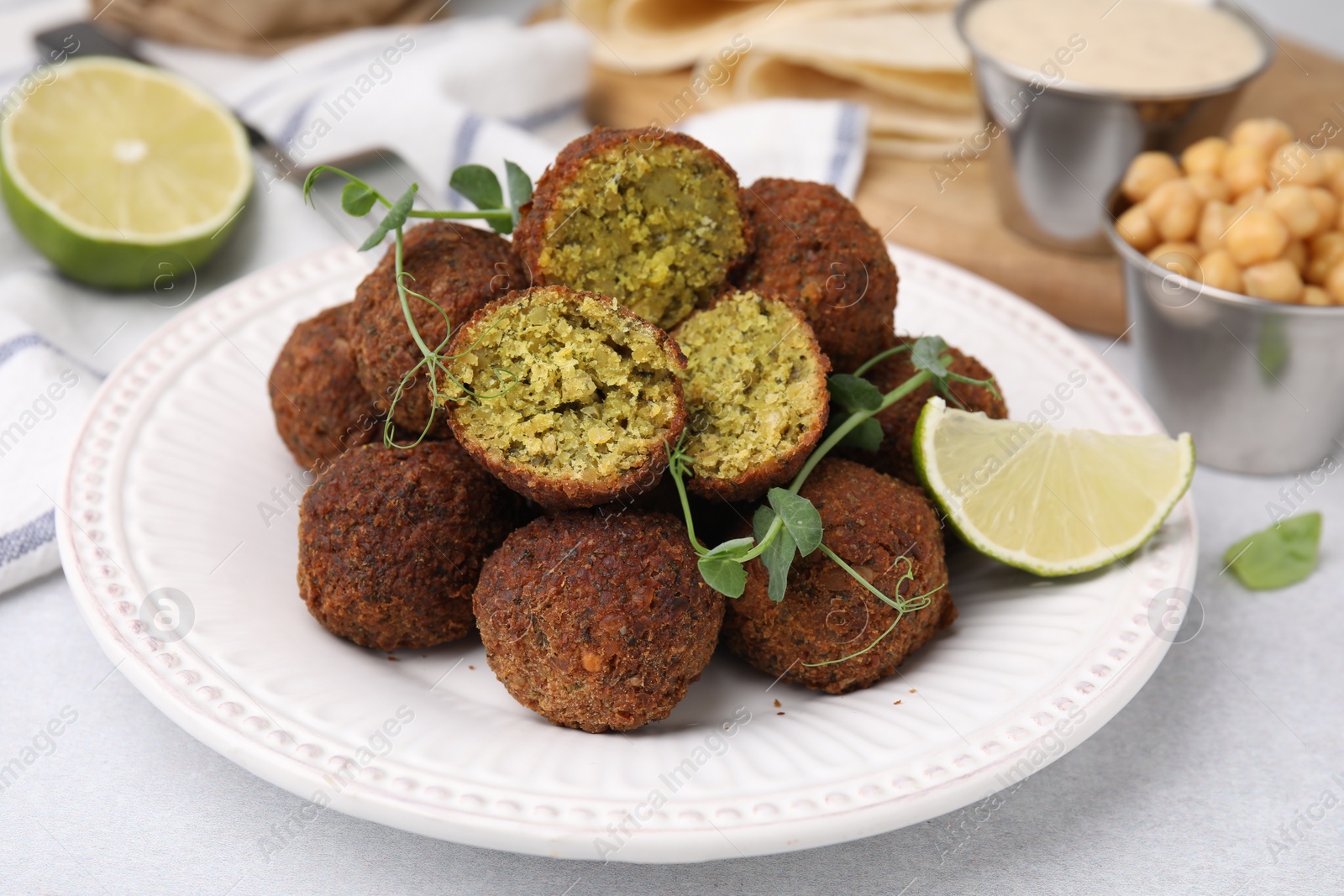 Photo of Delicious falafel balls, lime and microgreens on light table