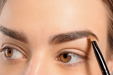 Photo of Young woman correcting eyebrow shape with brush, closeup