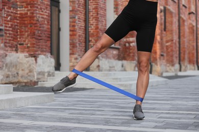 Photo of Woman doing exercise with fitness elastic band outdoors, closeup