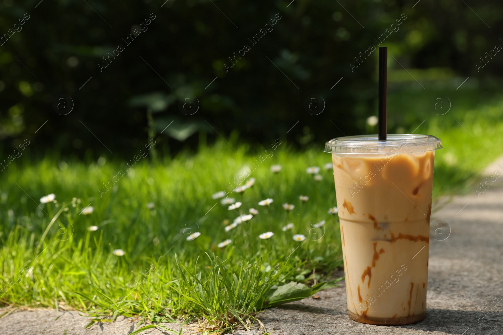Photo of Takeaway plastic cup with cold coffee drink and straw near green grass outdoors, space for text