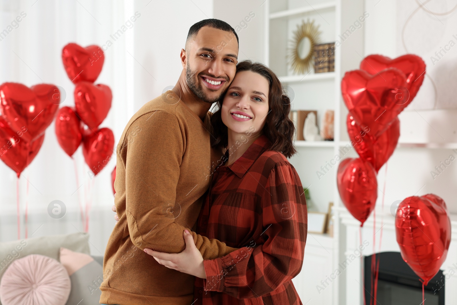 Photo of Lovely couple in room decorated with heart shaped air balloons. Valentine's day celebration