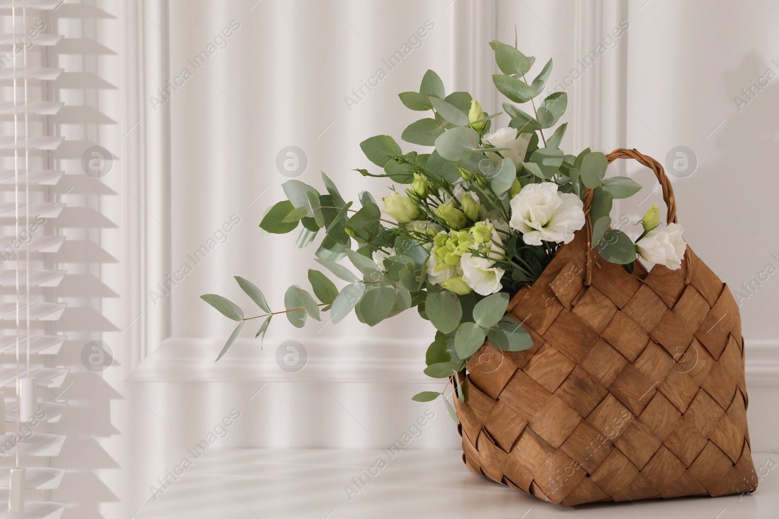 Photo of Stylish wicker basket with bouquet on white table indoors, space for text