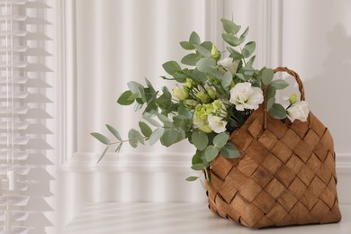 Photo of Stylish wicker basket with bouquet on white table indoors, space for text