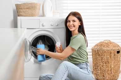 Photo of Woman pouring fabric softener into washing machine in bathroom