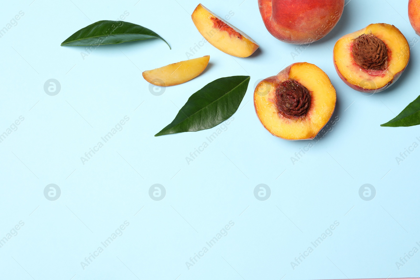 Photo of Delicious juicy peaches and leaves on light blue background, flat lay. Space for text