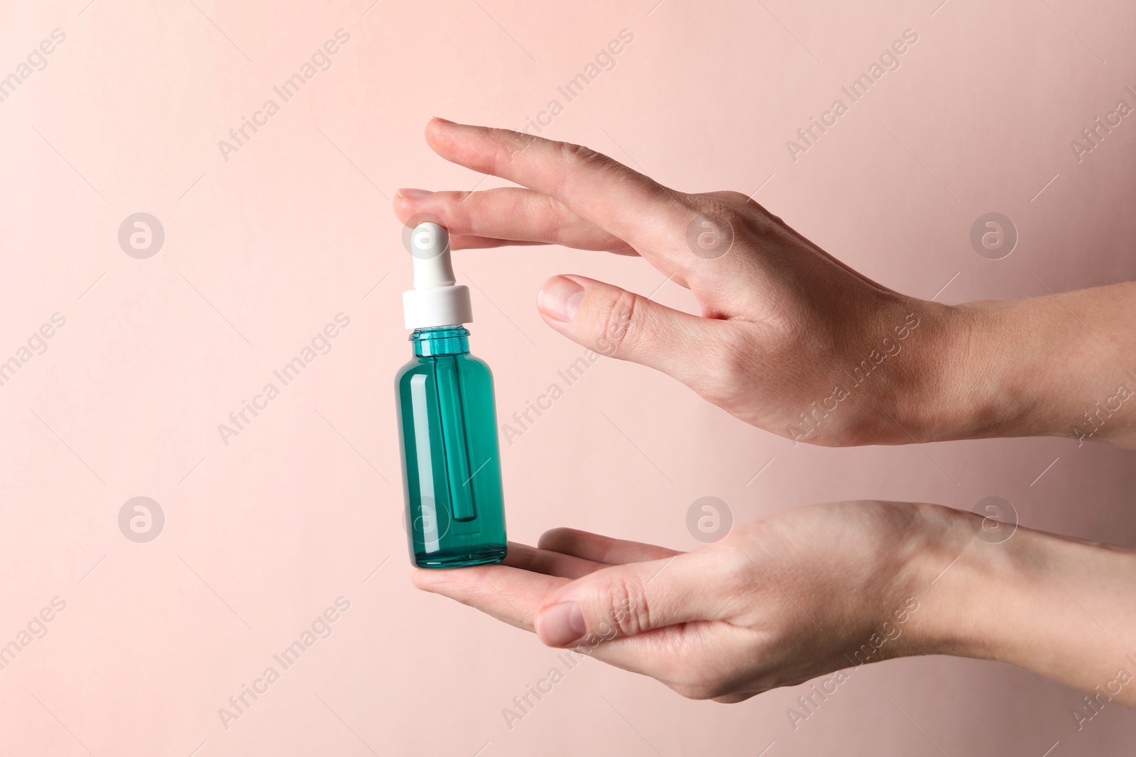 Photo of Woman with bottle of cosmetic serum on light pink background, closeup