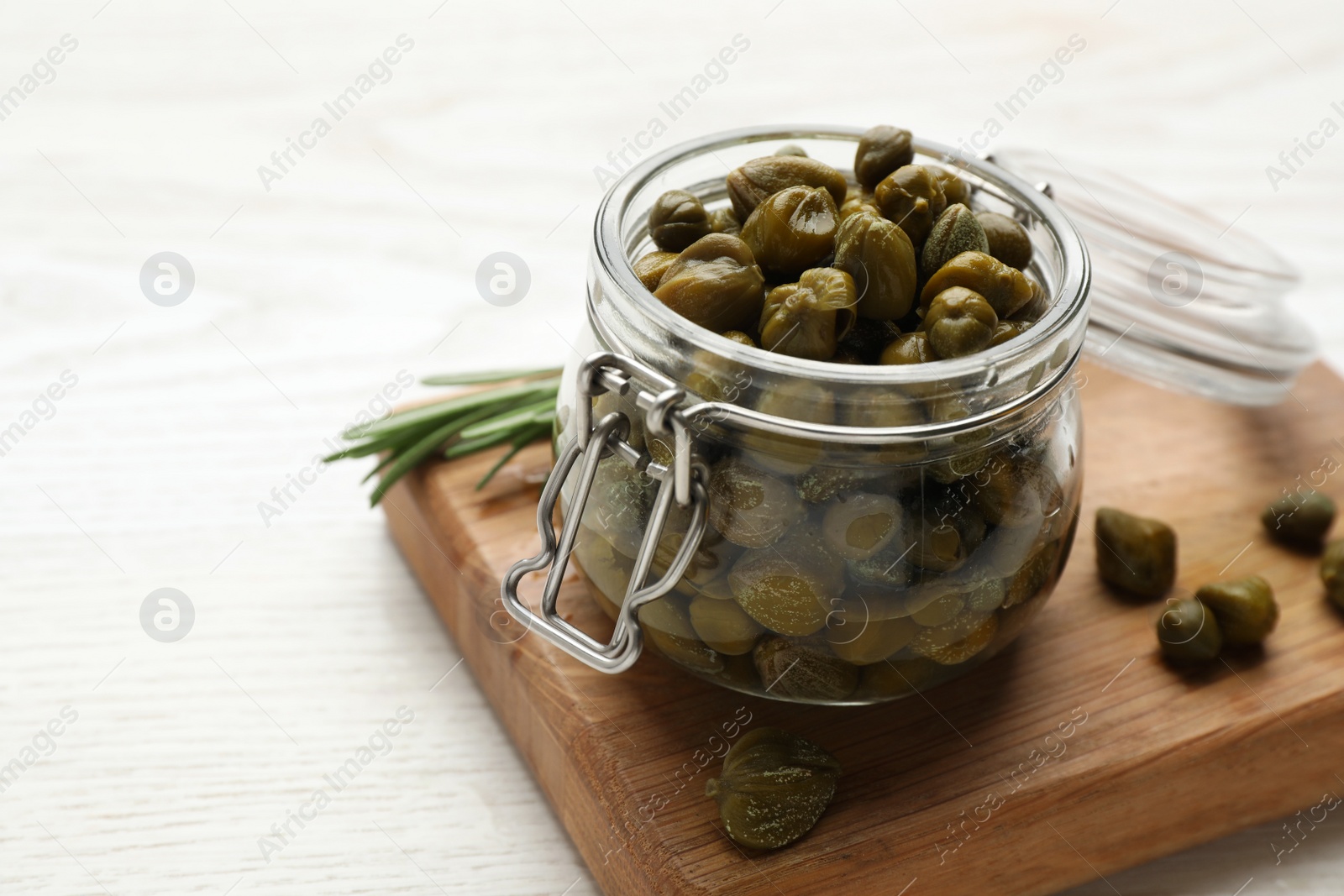 Photo of Jar with tasty capers and rosemary on white wooden table, space for text