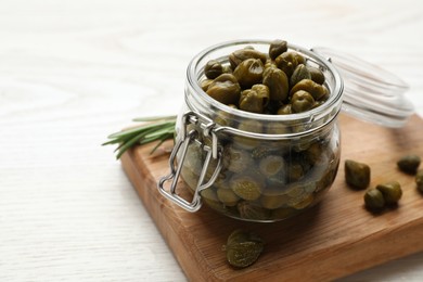 Jar with tasty capers and rosemary on white wooden table, space for text