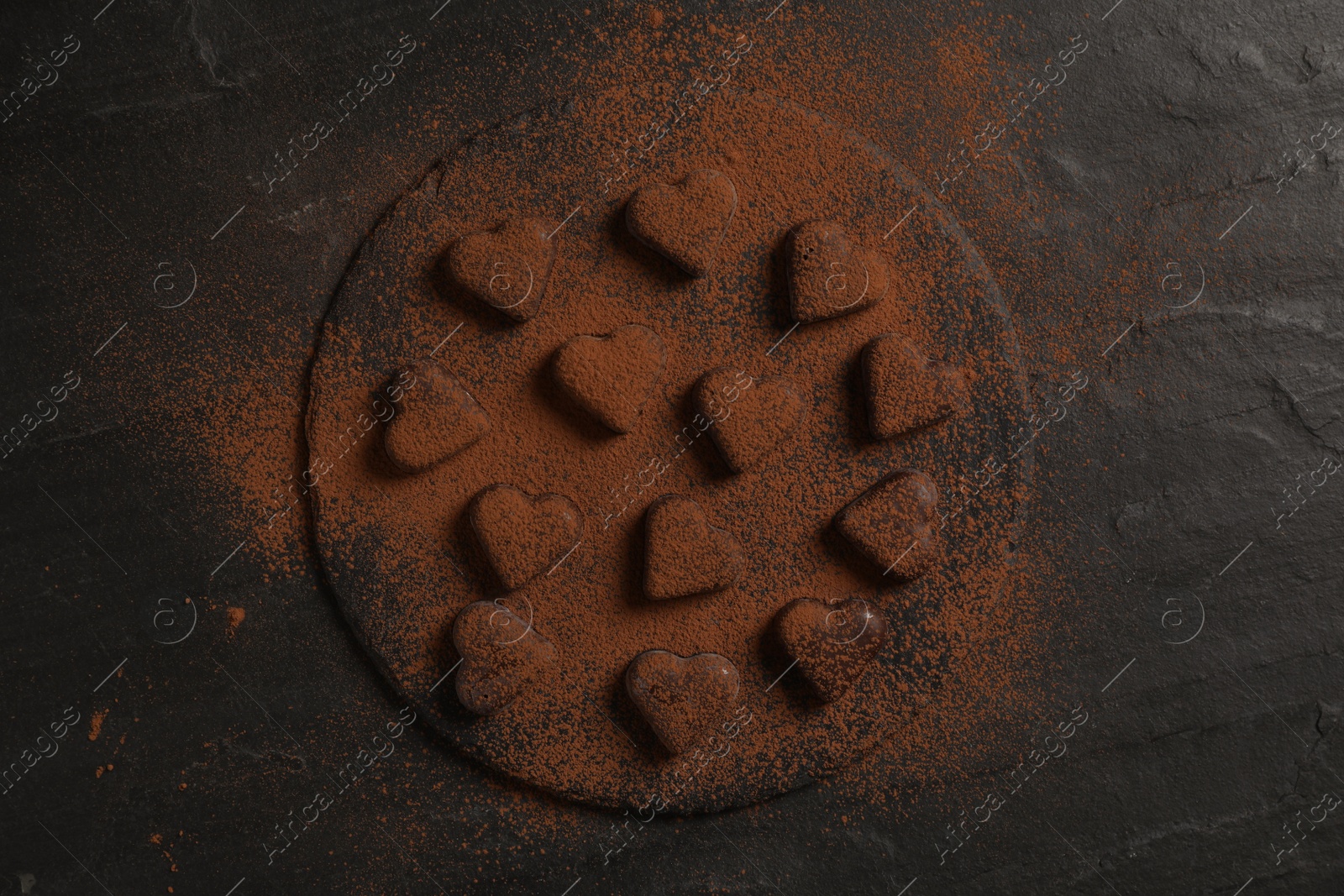 Photo of Beautiful heart shaped chocolate candies with cocoa powder on black table, top view