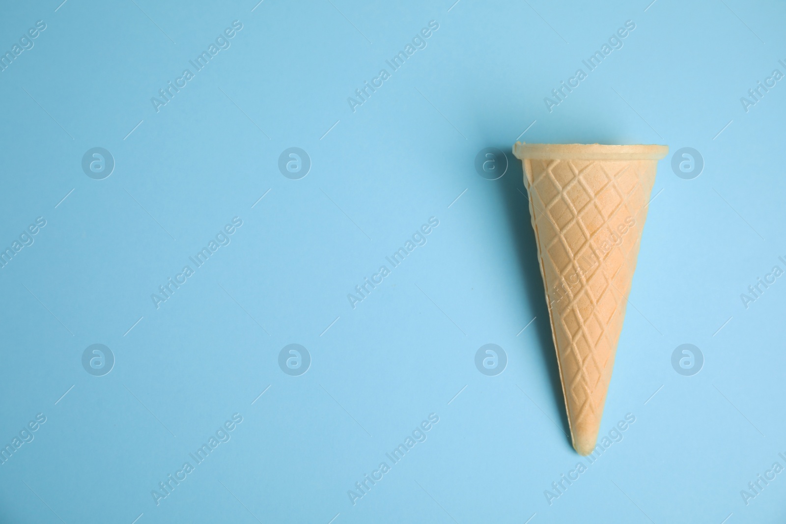 Photo of Empty wafer ice cream cone on blue background, top view. Space for text