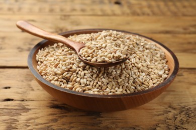 Dry pearl barley in bowl and spoon on wooden table, closeup