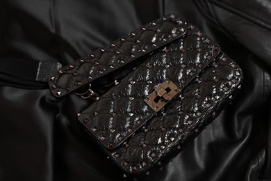 Photo of Stylish leather bag on black silk, closeup