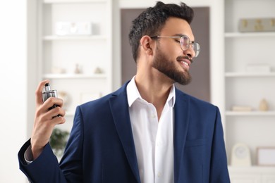 Photo of Attractive young man spraying luxury perfume indoors