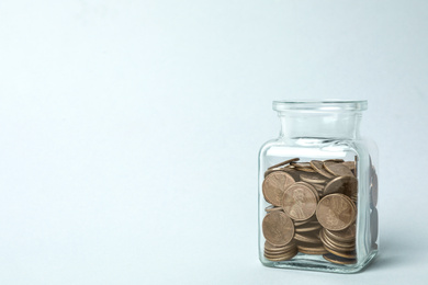 Photo of Glass jar with coins on light background, space for text