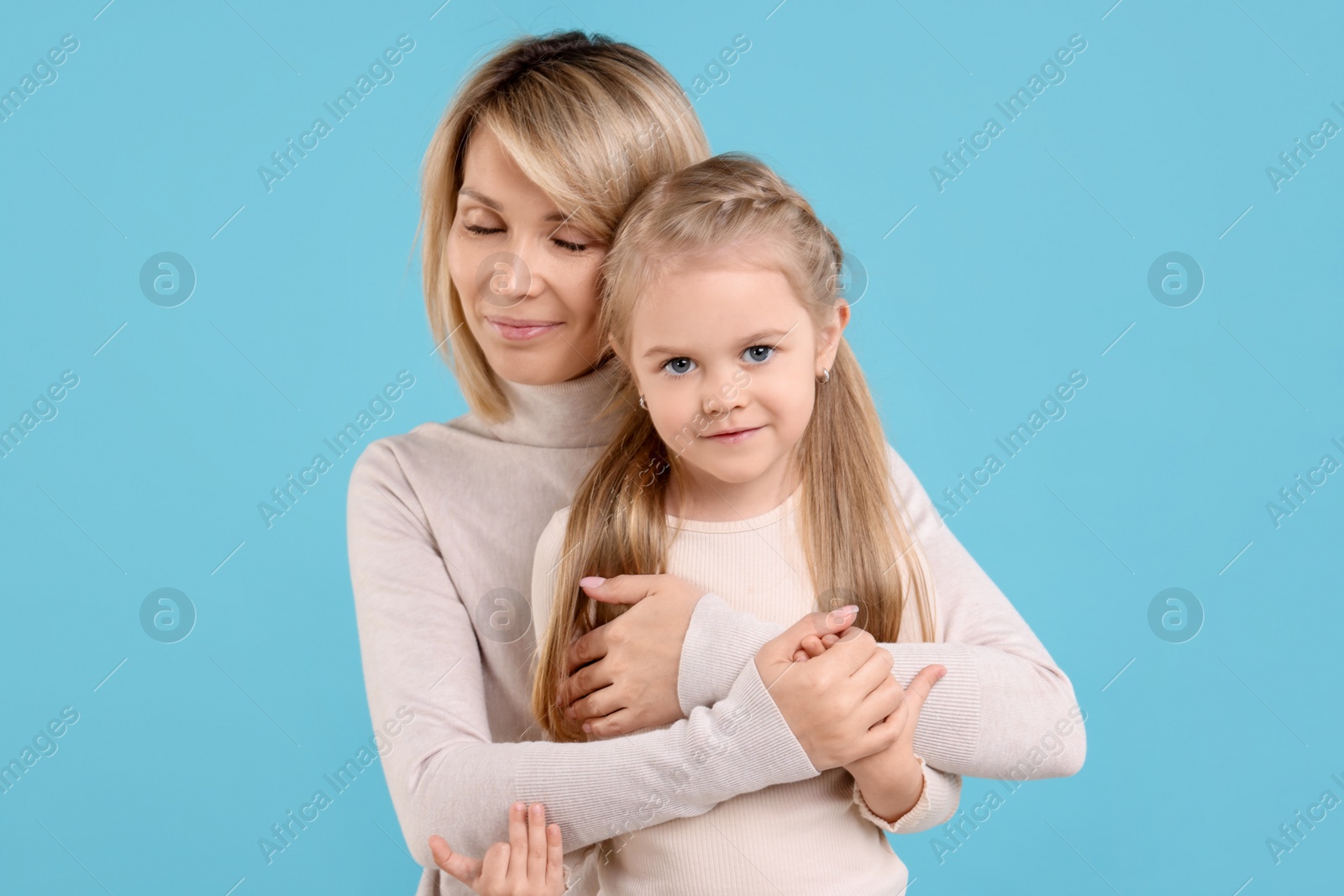 Photo of Mother hugging her daughter on light blue background