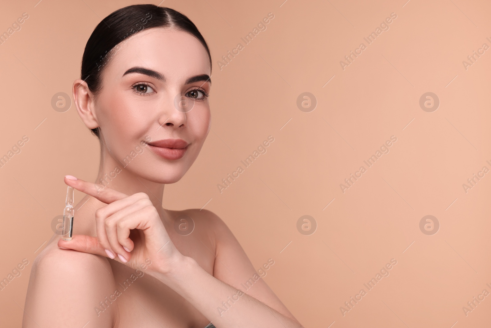 Photo of Beautiful young woman holding skincare ampoule on beige background. Space for text