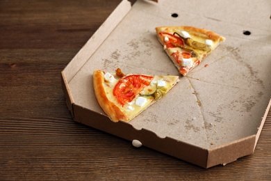 Cardboard box with tasty pizza slices on wooden background