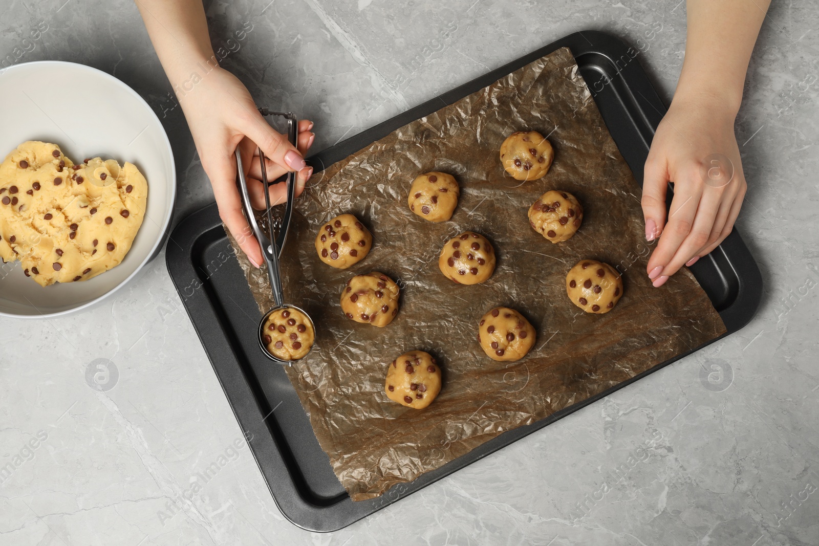 Photo of Woman making delicious chocolate chip cookies at light grey table, top view