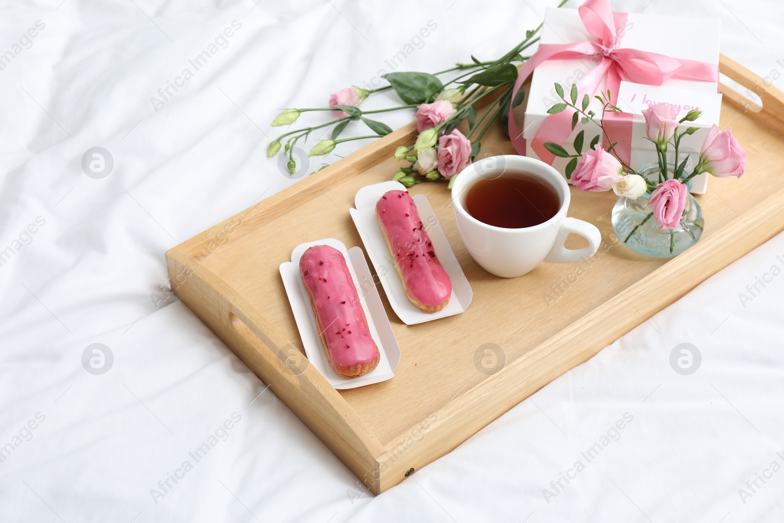 Photo of Tasty breakfast served in bed. Delicious eclairs, tea, gift box, flowers and card with phrase I Love You on tray