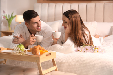 Photo of Happy couple in bathrobes having breakfast on bed at home