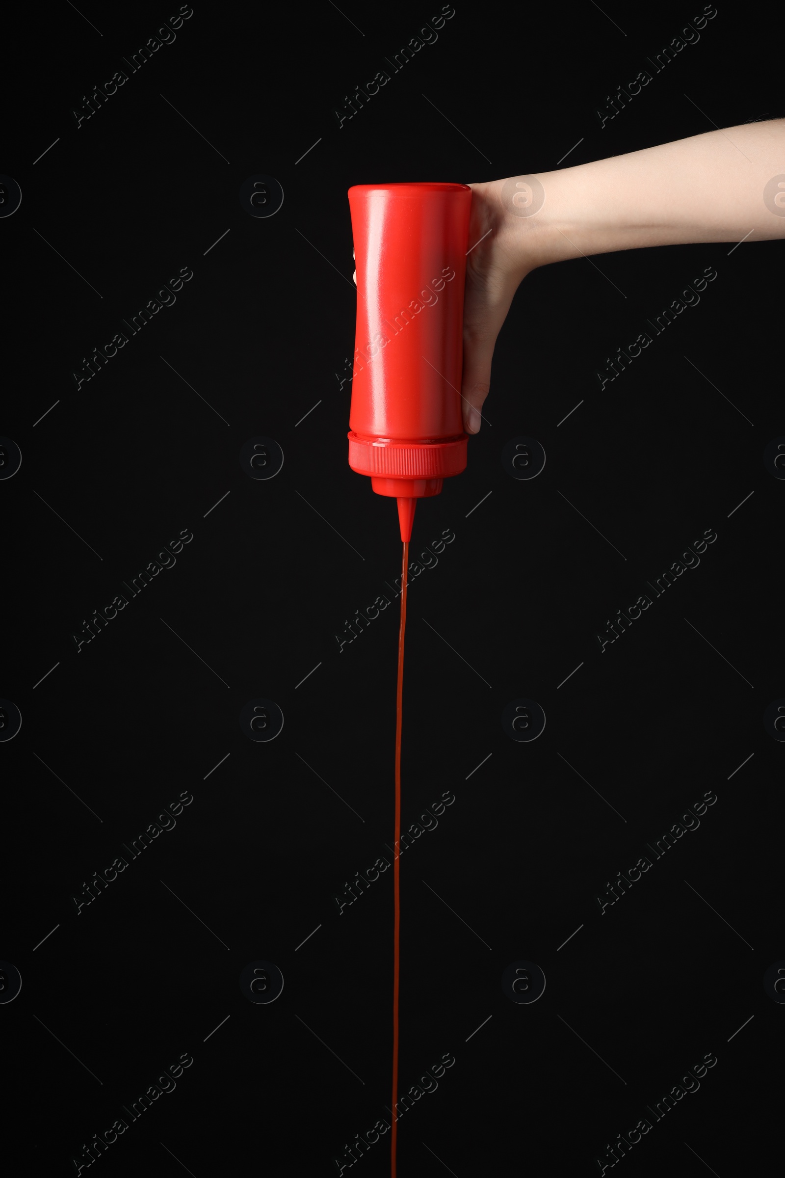 Photo of Woman pouring tasty ketchup from bottle on black background, closeup