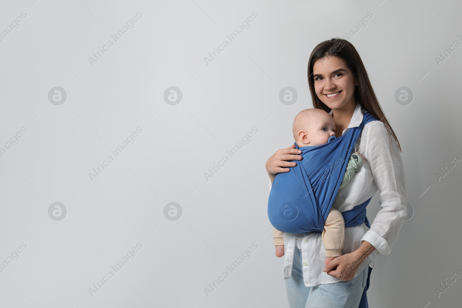 Photo of Mother holding her child in sling (baby carrier) on light grey background. Space for text